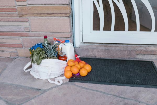 Reusable bag with groceries and fruits left at doorstep, highlighting delivery service.